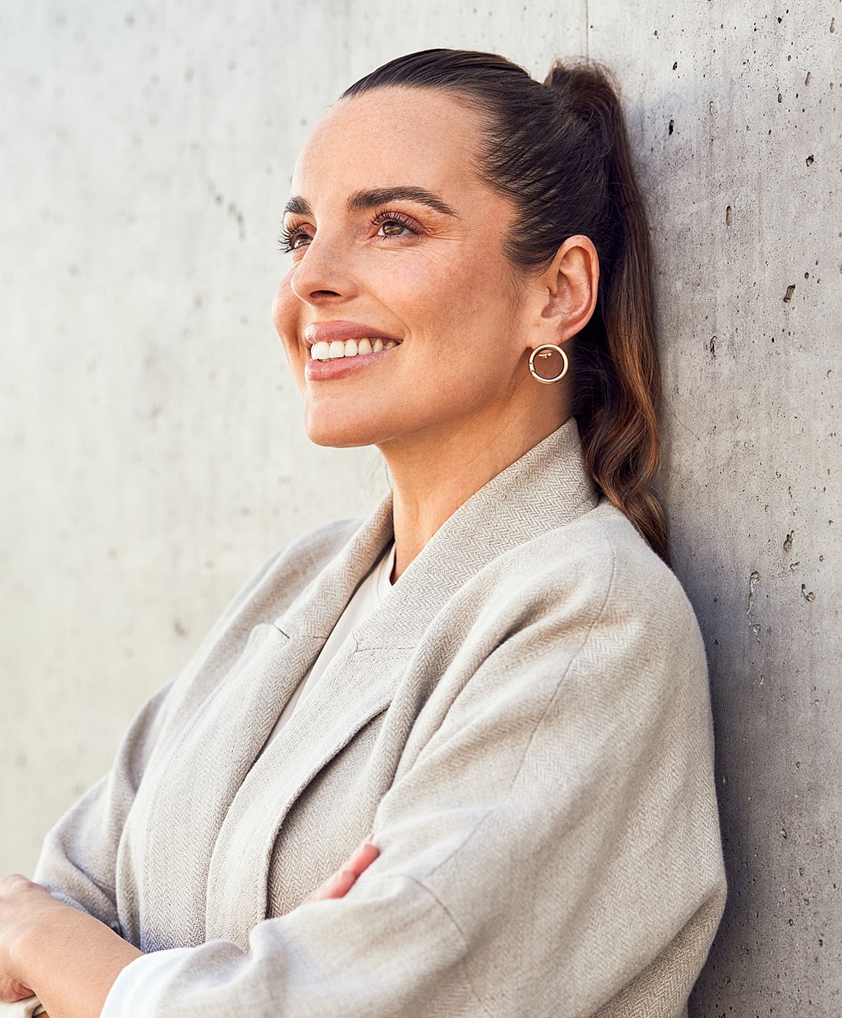 Smiling Melbourne Botox model leaning against a concrete wall.