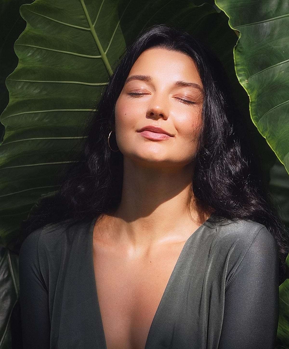 Melbourne facial model with closed eyes surrounded by green leaves