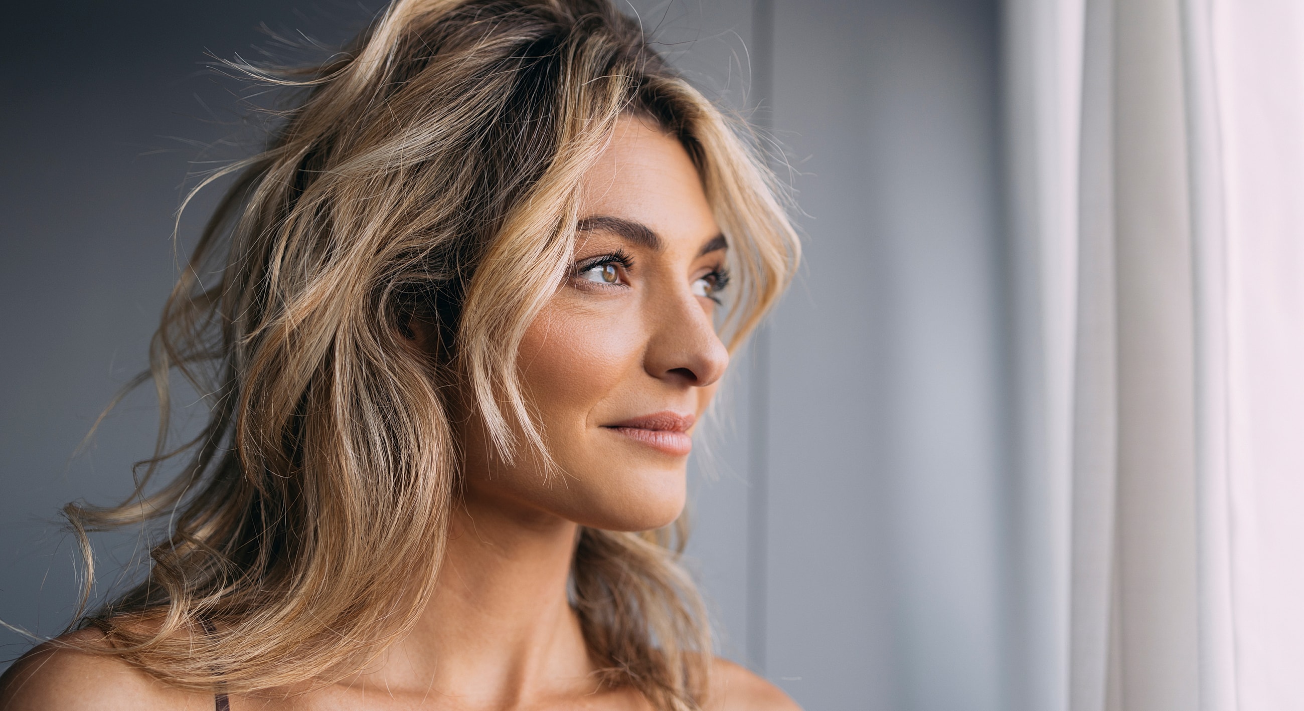Melbourne weekend facelift model gazing out a window with light background.