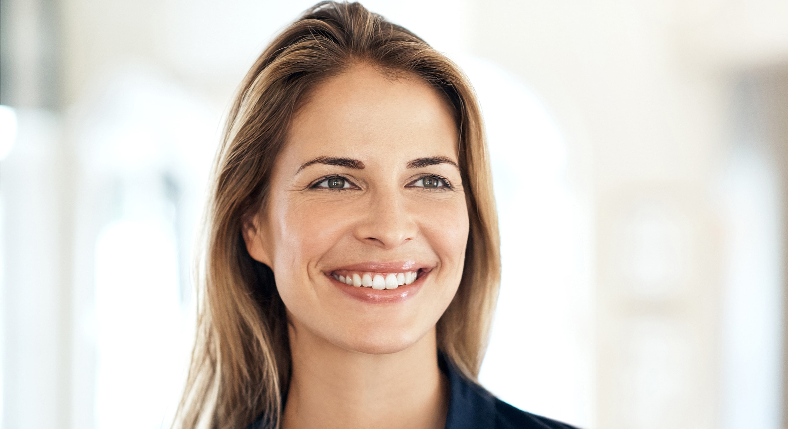 Smiling Melbourne blepharoplasty model with long hair in bright setting.