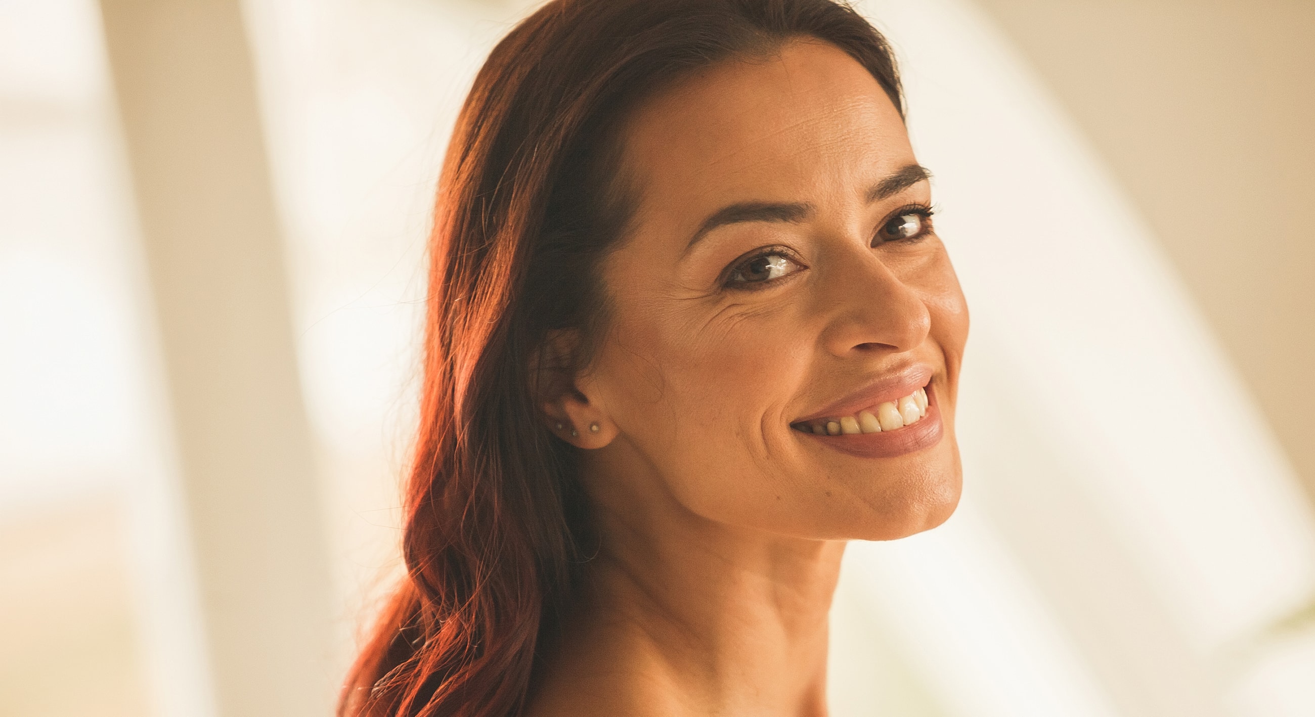 Smiling Melbourne brow lift model with long, dark hair indoors.
