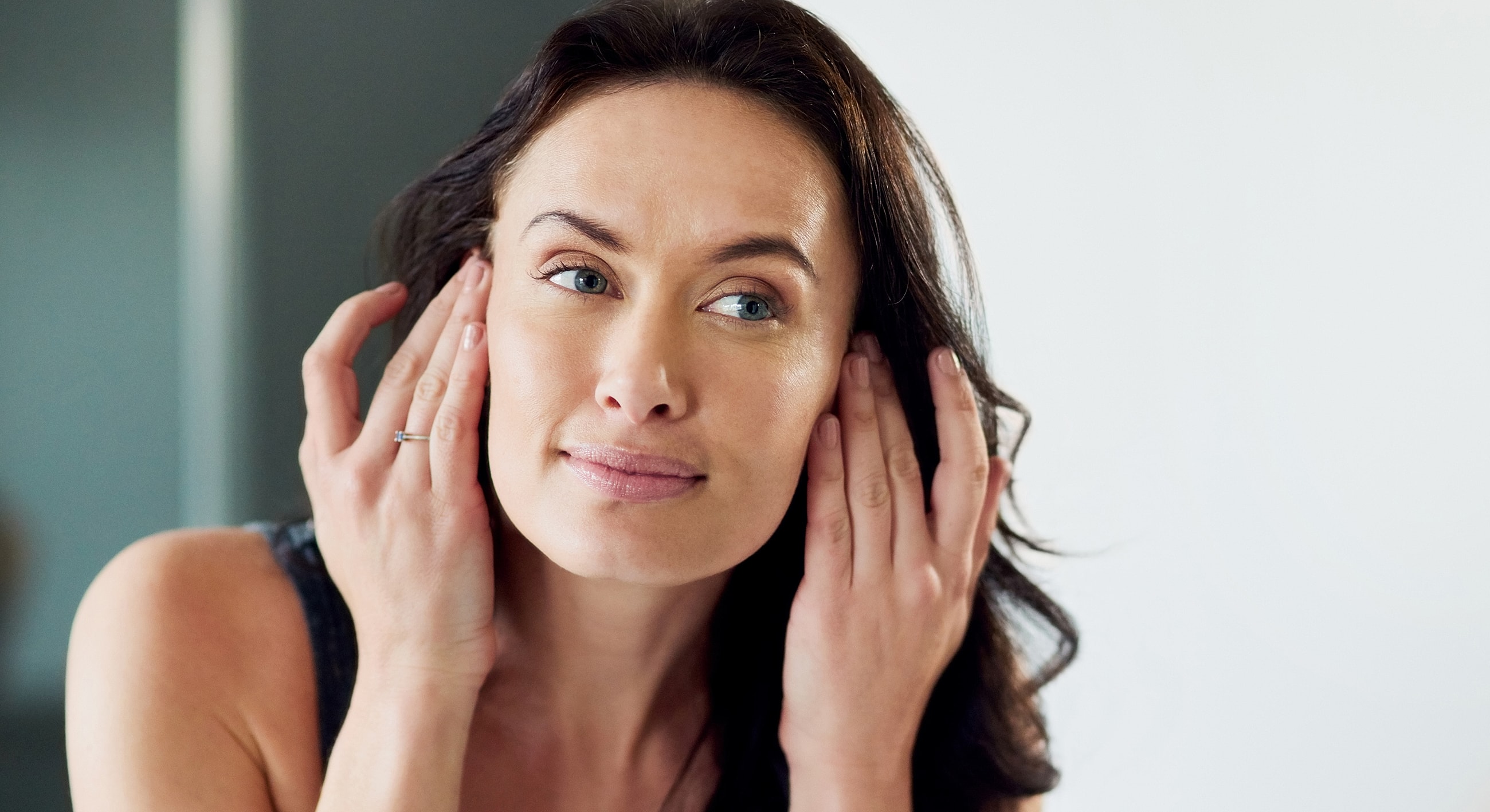Melbourne microneedling model applying skincare in front of a mirror.